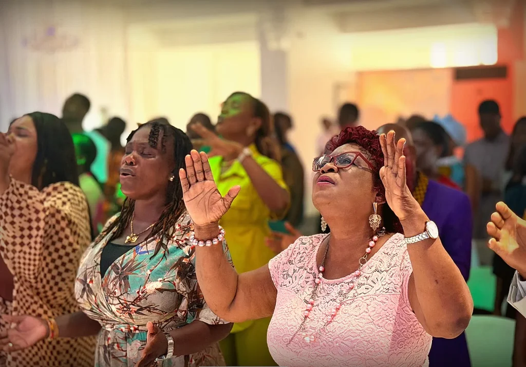 Members worshipping with hands raised, eyes closed in prayer