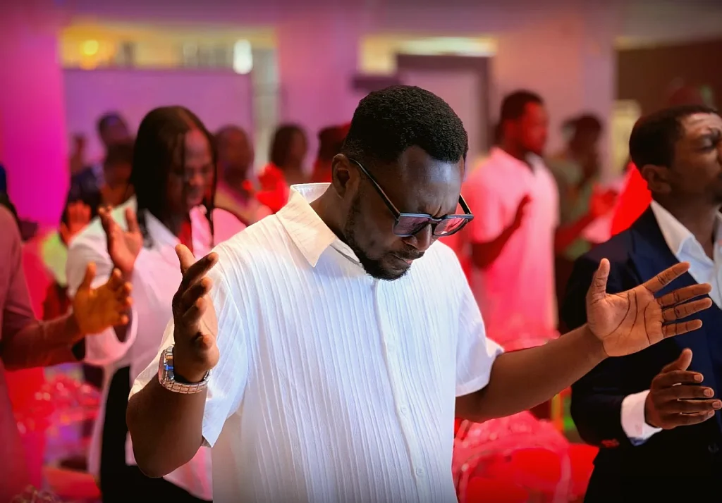 A worshipper with hands raised in praise under pink and red stage lighting